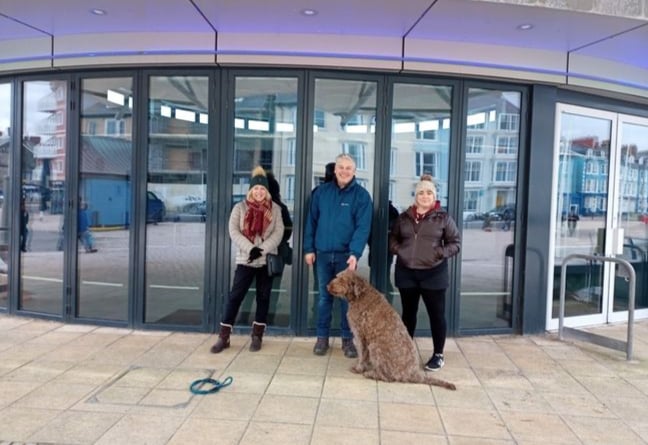 Caru Aber members Christine Copeland, Jeff Jones, and Bethan Thomas standing outside Aberystwyth bandstand, where the CANU ABER gyda CARU ABER music event will take place.