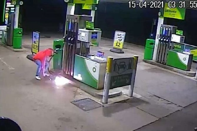 A CCTV still of a person lighting a puddle of petrol.