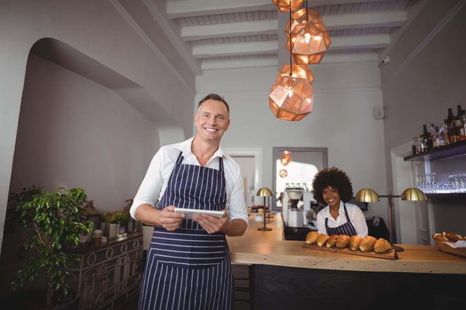 Waiter holding digital tablet while waitress smiling in background at counter in restaurant