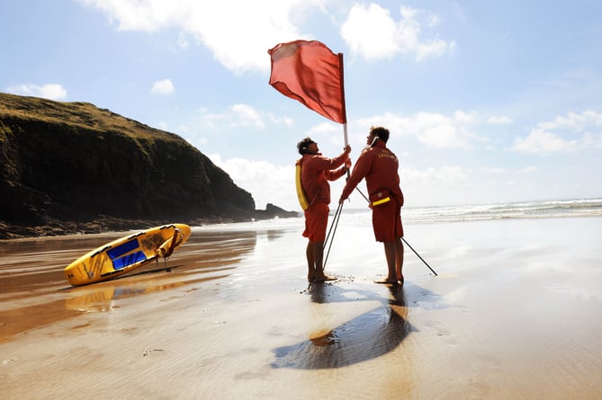 Two lifeguards putting out a red flag on a beach in Pembrokeshire.