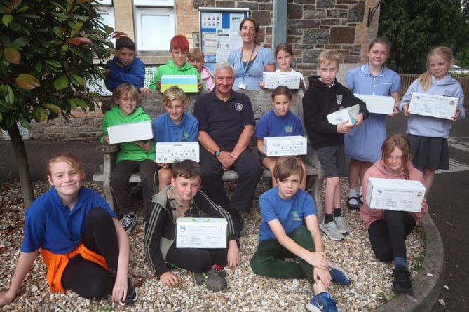 With some of the filled shoeboxes for Ukraine, pupils who were leaving Yeoford that day to go up to senior school, with Rotary Club of Crediton Boniface member Nick Yarnold and headteacher Vicki Gillon.  SR 5567

